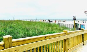 Ein Strand mit einer Holzpromenade, einem Schild mit der Aufschrift 'KEEP OFF DUNES' und Menschen, die den Strand genießen.