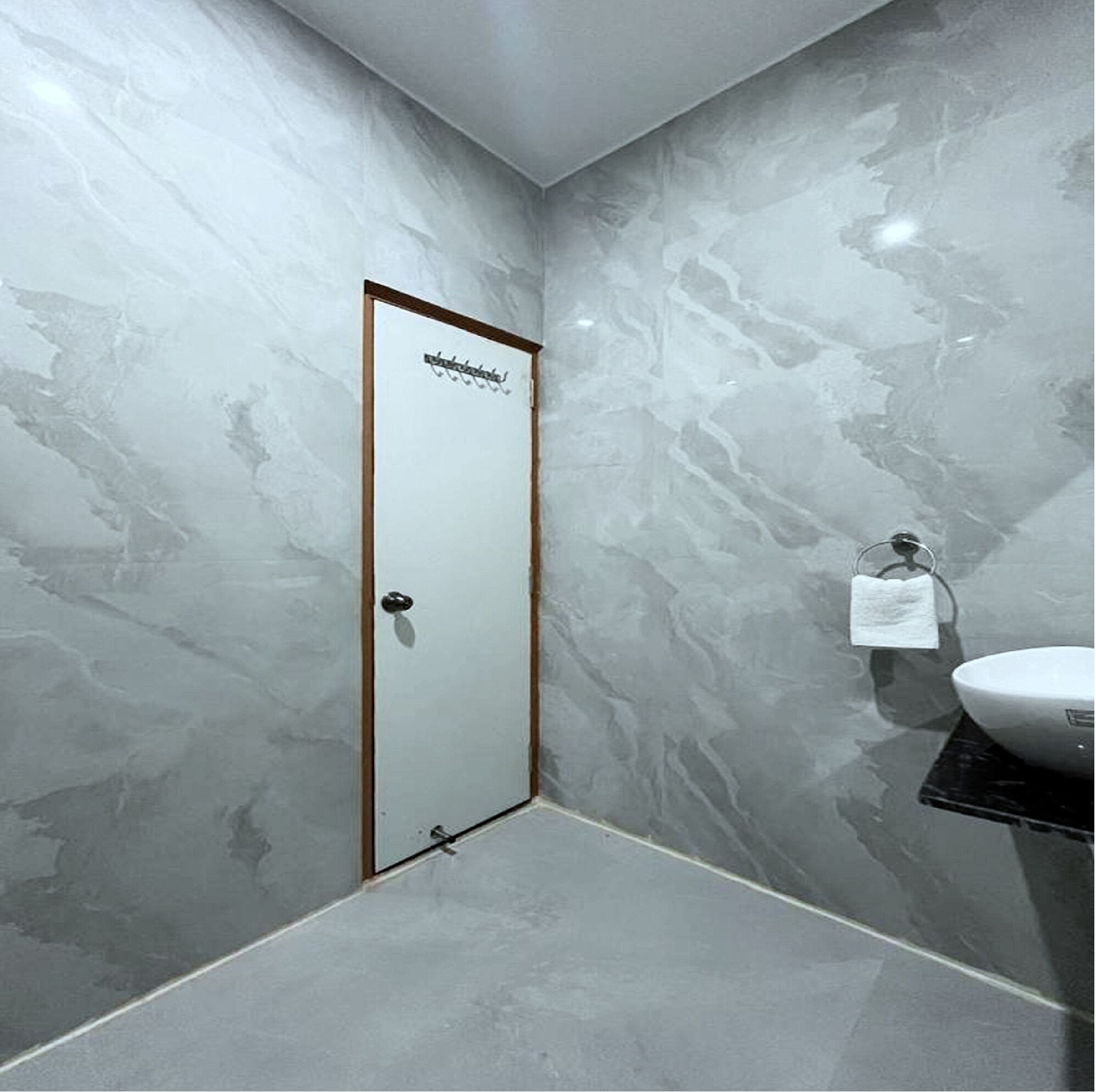 A bathroom with a marble wall, a white door, a sink, and a towel rack.