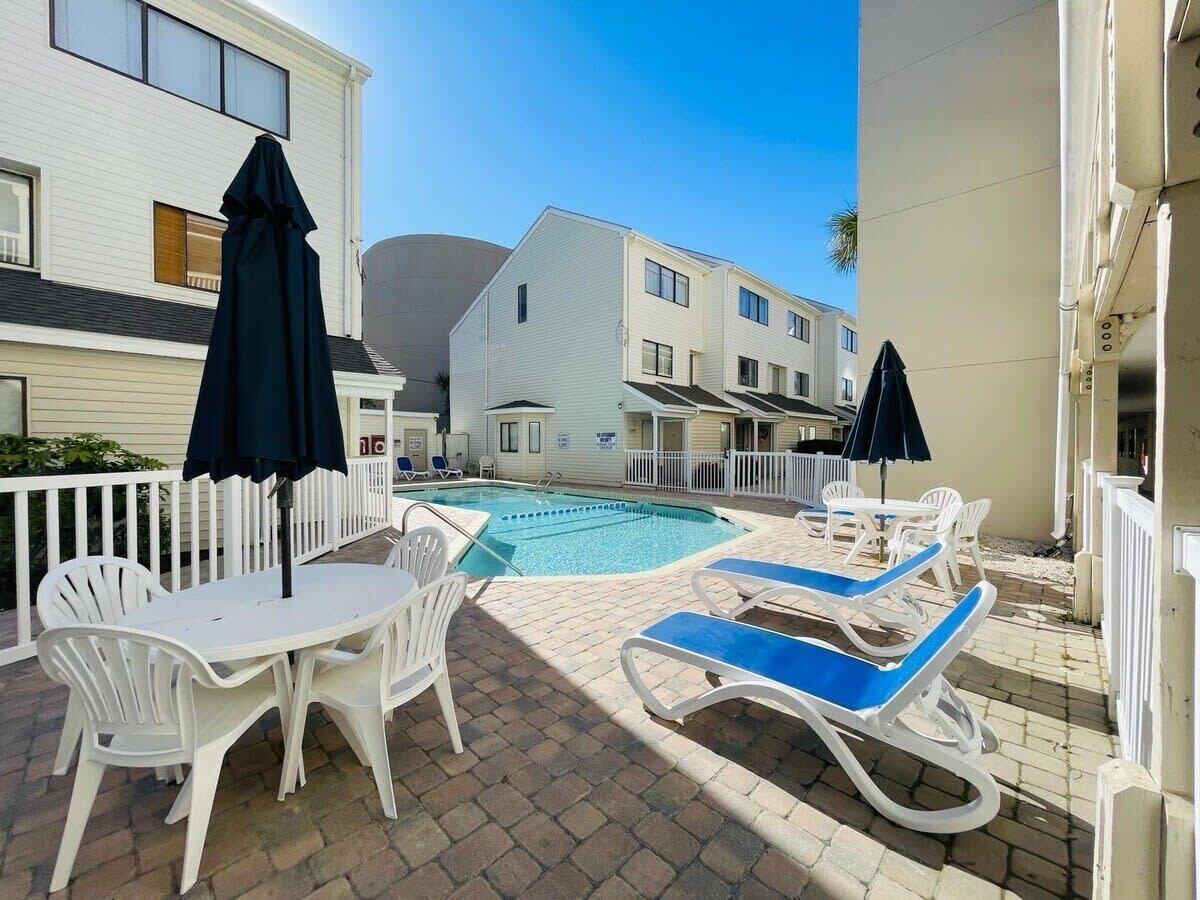 A pool area with lounge chairs and a table, surrounded by a white fence.