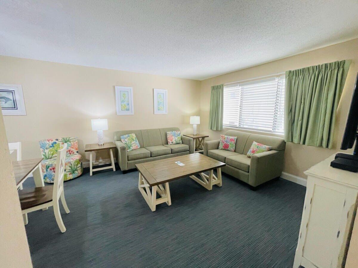 A furnished living room with a sofa set, a coffee table, a dining table with chairs, and a cabinet.