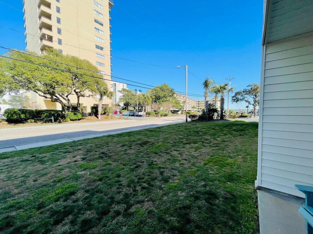 A grassy yard with a sidewalk and a tall building in the background.
