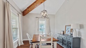 A dining area with a wooden table and white chairs, a blue cabinet with drawers, and a hanging light fixture.