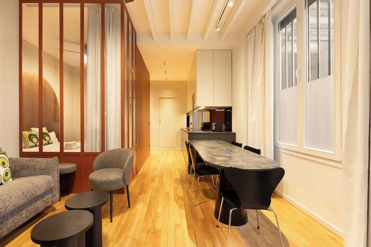 Una sala moderna con un sofá, sillas, una mesa de comedor y una cocina al fondo.