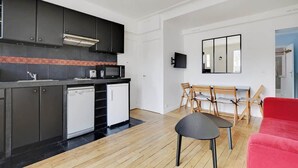 A compact kitchen with dark cabinets, a microwave, and a dishwasher. There is a dining area with a table and chairs, and a red sofa. - An Amazing 2-BR/1BA in Ternes - Arc de Triomphe (Paris)