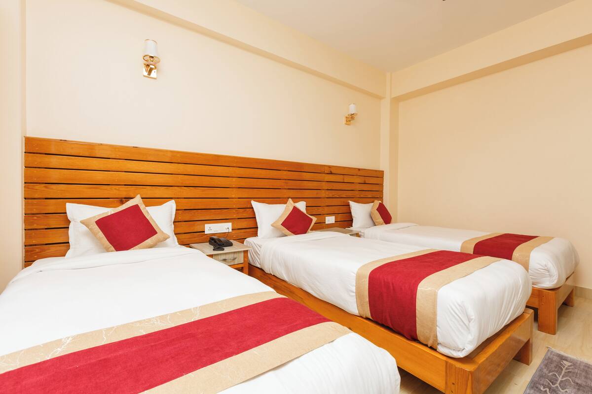A hotel room with three single beds, wooden headboards, white bedding, and red accents.