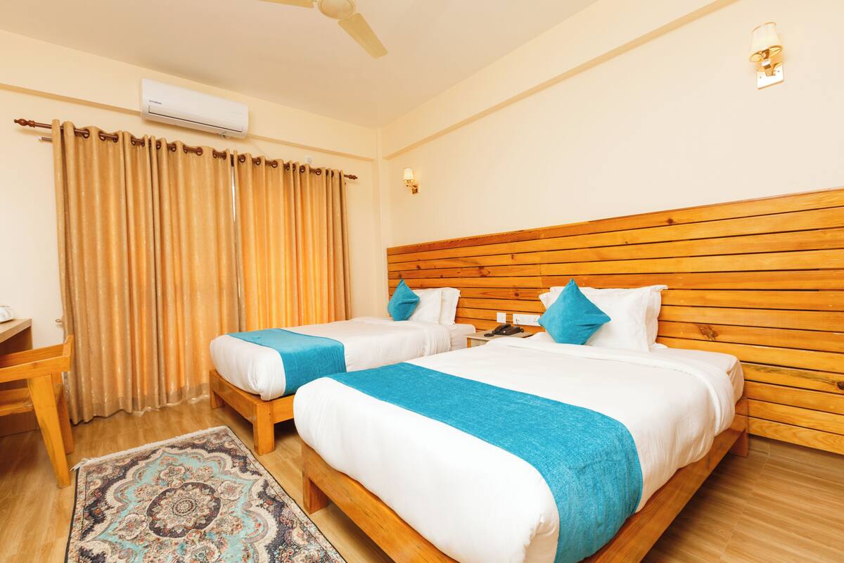 A hotel room with two beds, a wooden headboard, a desk, and a patterned rug.