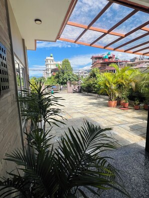 A covered outdoor area with potted plants, a tiled floor, and a view of surrounding buildings. - Shekhar's Place (Pokhara)