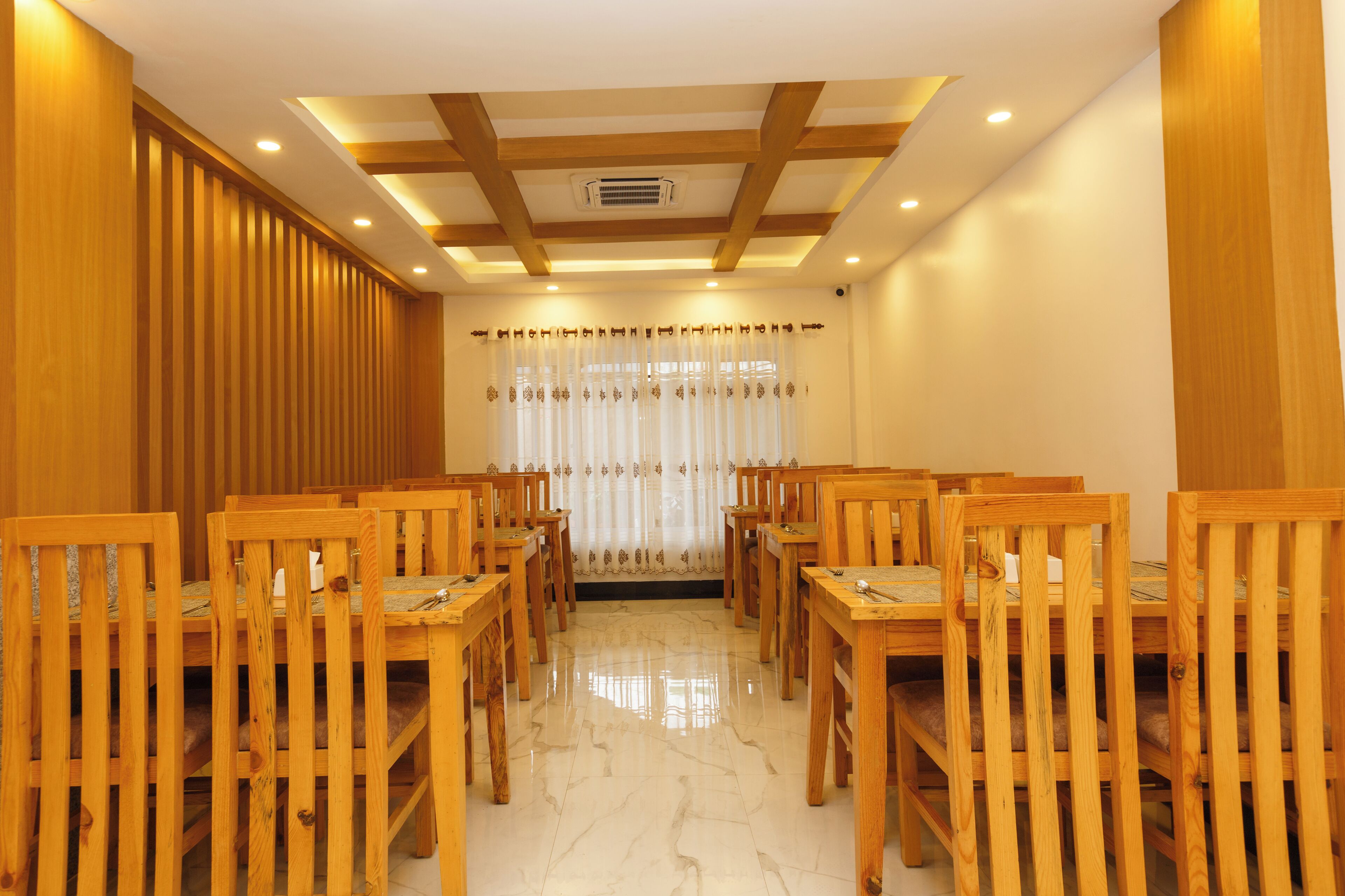 Un espace repas avec des tables et des chaises en bois, un sol en marbre et un plafond doté d’un éclairage encastré et de poutres en bois.