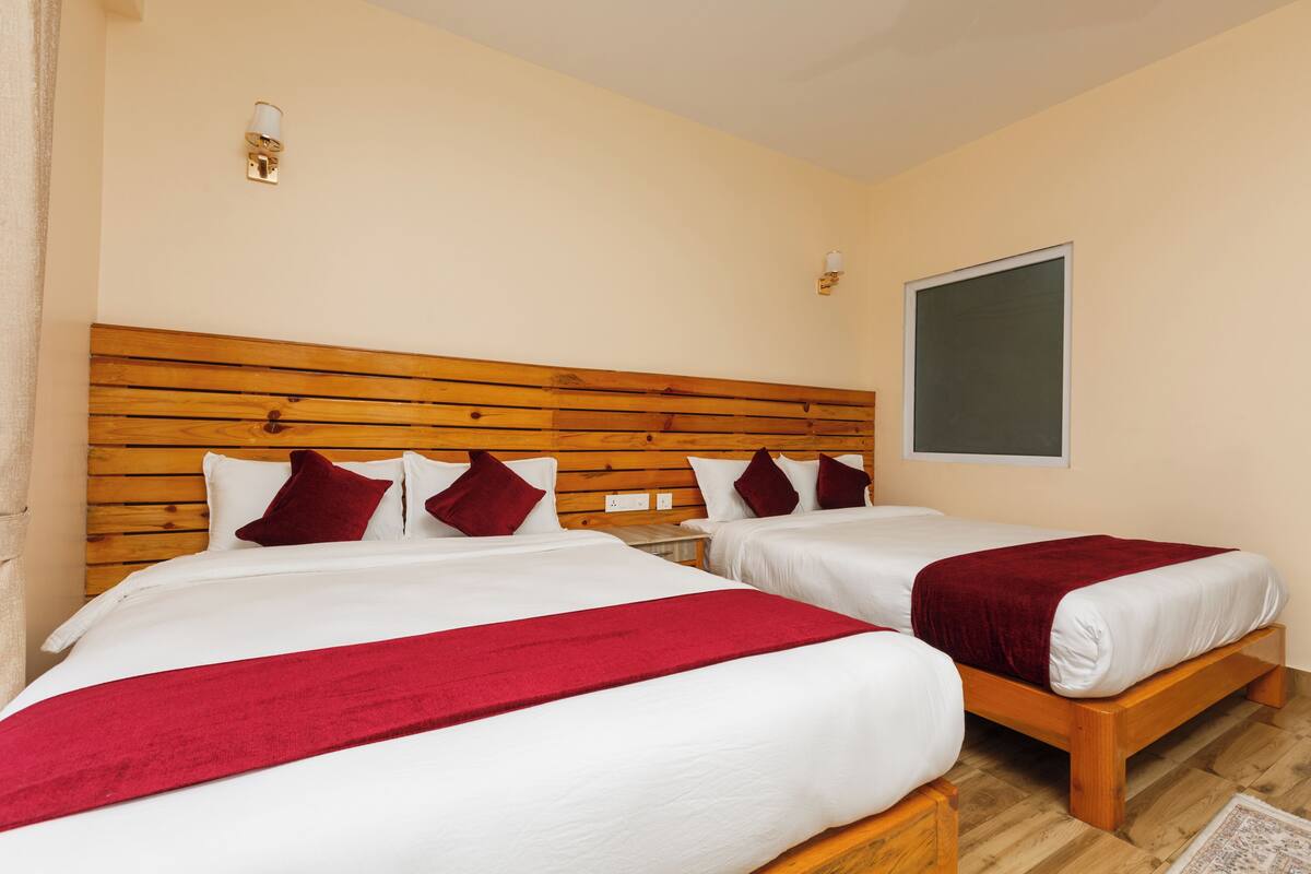 A hotel room with two beds, wooden headboards, white bedding, red throw blankets, and wall-mounted light fixtures.