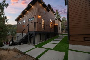 A modern two-story house with a wooden exterior, a staircase leading to the upper level, and a well-maintained lawn with a concrete pathway. - Luxury Home with Lake Views, Hot Tub, AC, Game Room & Walk to Village (Big Bear Lake)