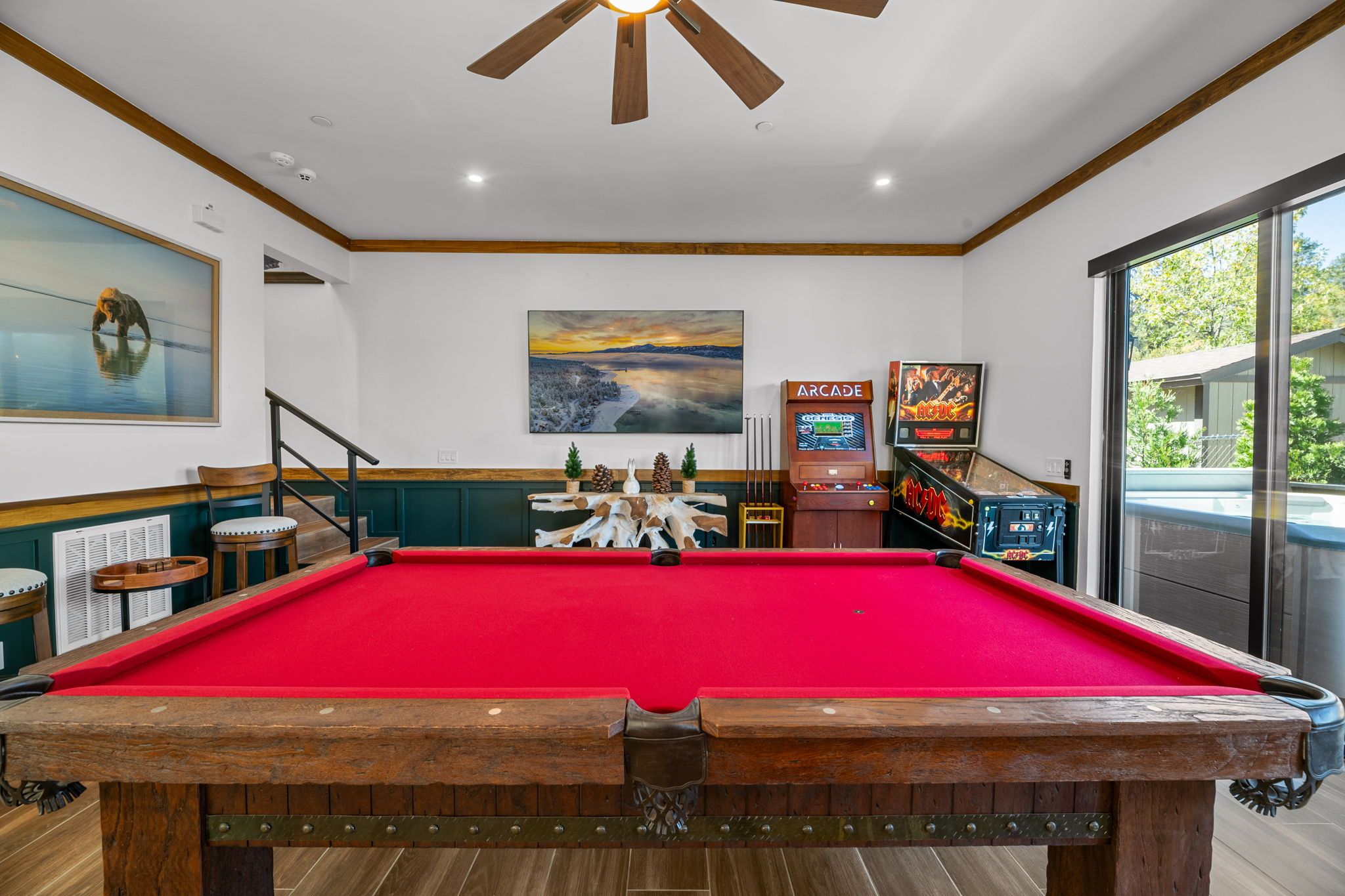 A pool table with a red felt surface, wooden surroundings, and a ceiling fan.