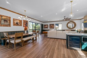Une cuisine moderne dotée d’un four encastré, d’un coin repas avec des chaises et un banc en bois, et d’une grande fenêtre offrant une vue sur l’extérieur.