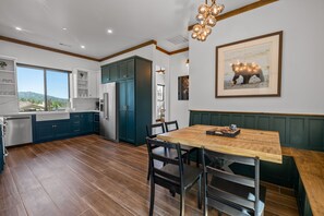 Een moderne keuken met donkerblauwe kastjes, een houten eettafel en een groot raam met uitzicht op het landschap.