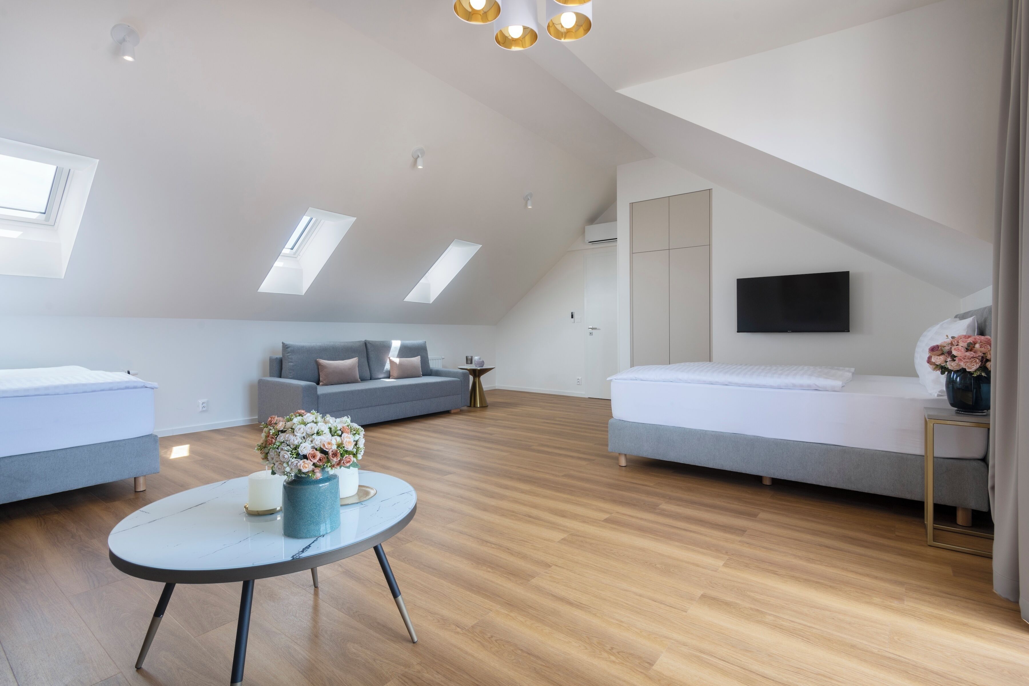 Een moderne loft slaapkamer met dakraam, een bank, een bed en een kleine tafel met bloemen.