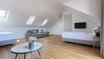 Quarto tipo loft moderno com claraboia, sofá, cama e uma pequena mesa com flores.