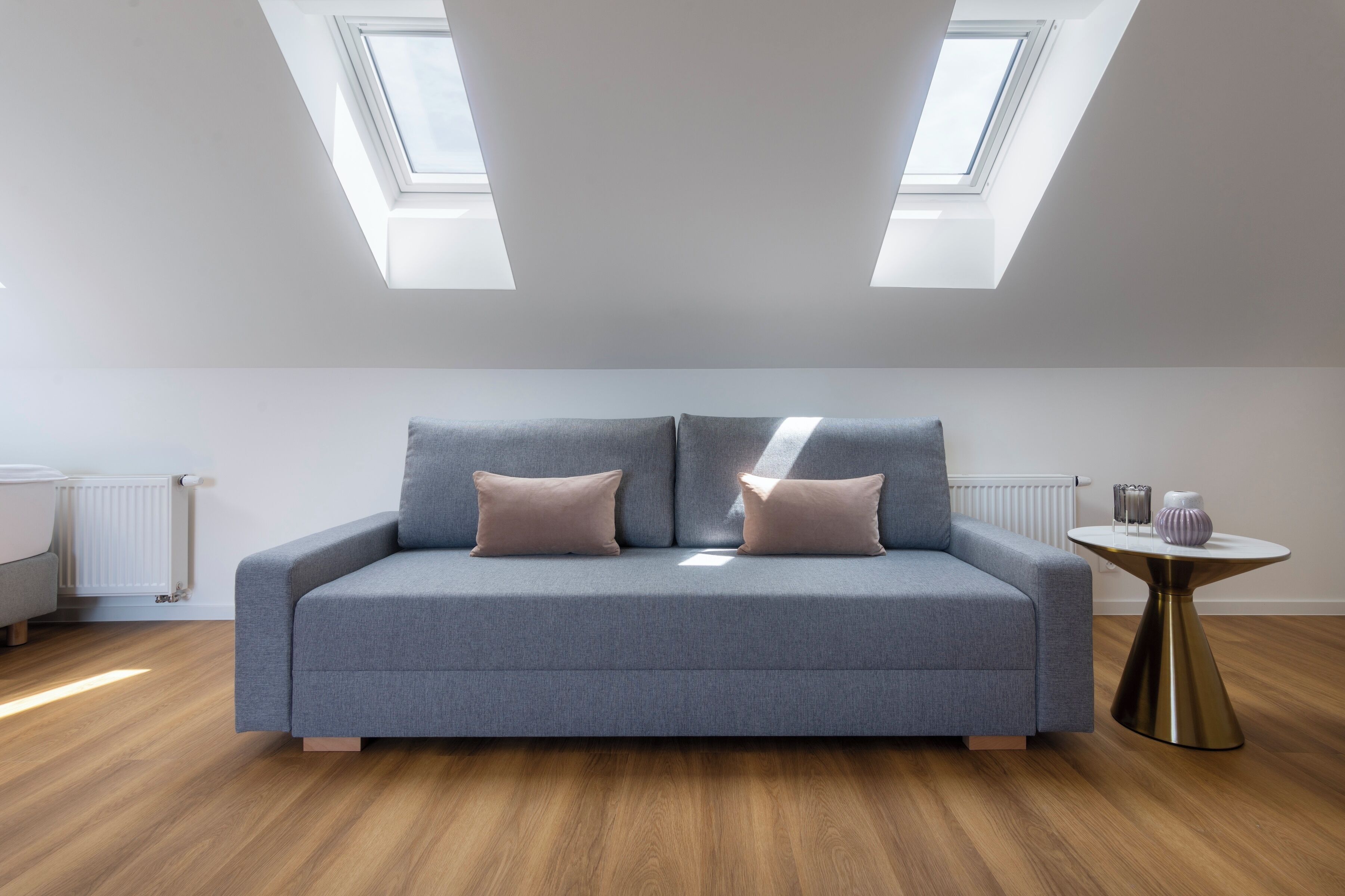 Une chambre de style loft moderne, avec un canapé gris, deux fenêtres de toit, une table ronde et un plancher en bois.