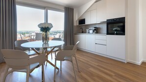 A modern kitchen with white cabinets, a black oven, and a dining area with a round table and chairs. - Encore Boutique Residence by Dwellfort (Prague)
