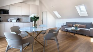 A modern kitchen with white cabinets, a dining area with a glass table and chairs, and a living area with a sofa and coffee table. - Encore Boutique Residence by Dwellfort (Prague)