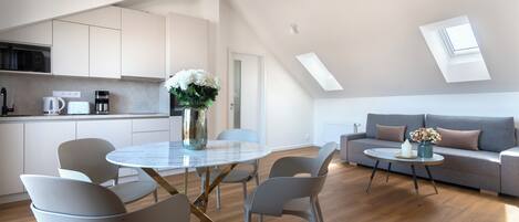 A modern kitchen with white cabinets, a dining area with a glass table and chairs, and a living area with a sofa and coffee table.