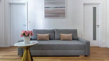 Un salon moderne avec un canapé gris, une petite table ronde dotée d’un pied doré et un vase rempli de fleurs roses.
