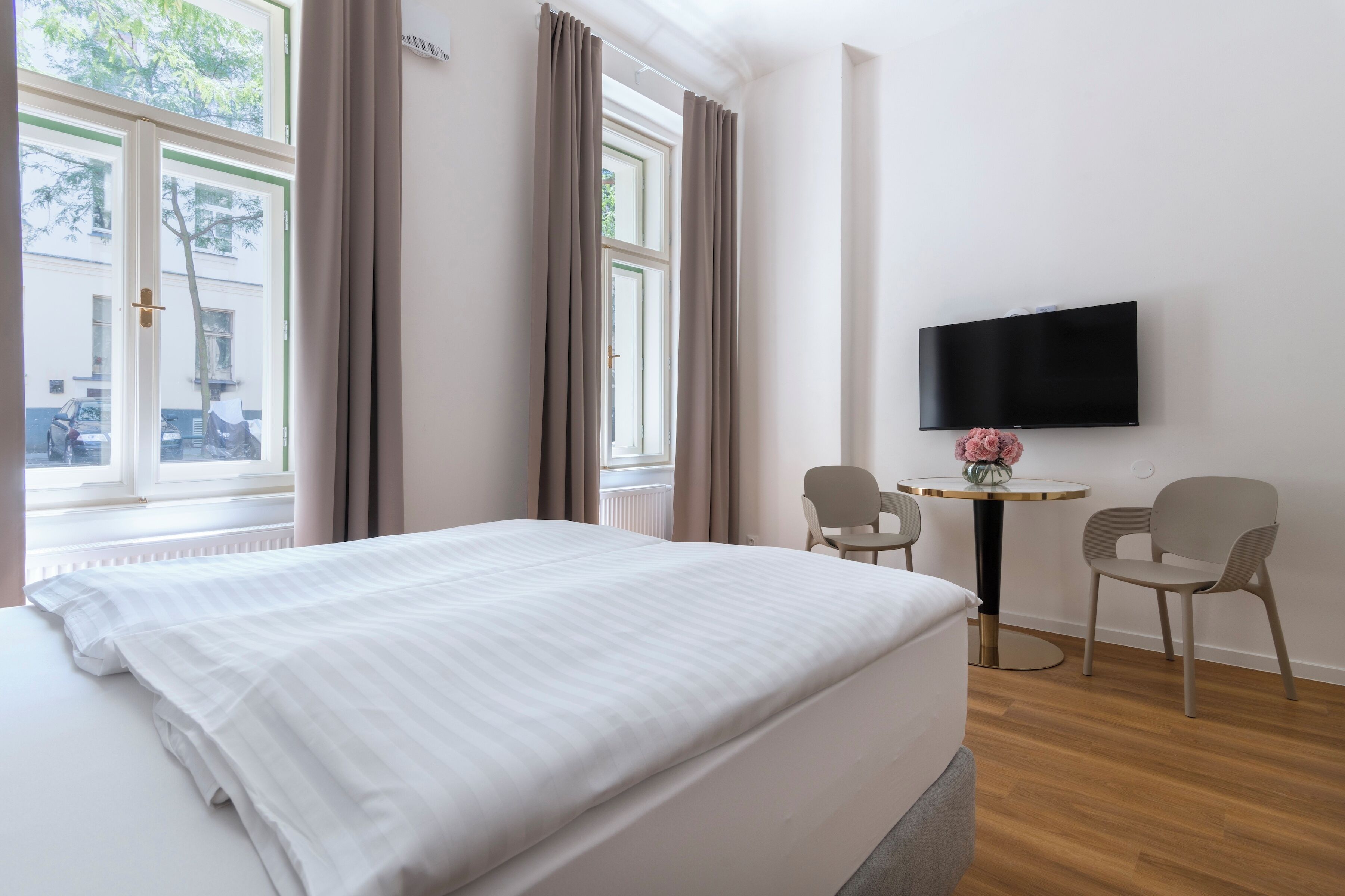 Habitación de hotel con una cama, dos sillas, una mesita y un televisor en la pared.