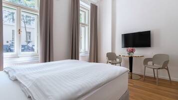 Habitación de hotel con una cama, dos sillas, una mesita y un televisor en la pared.