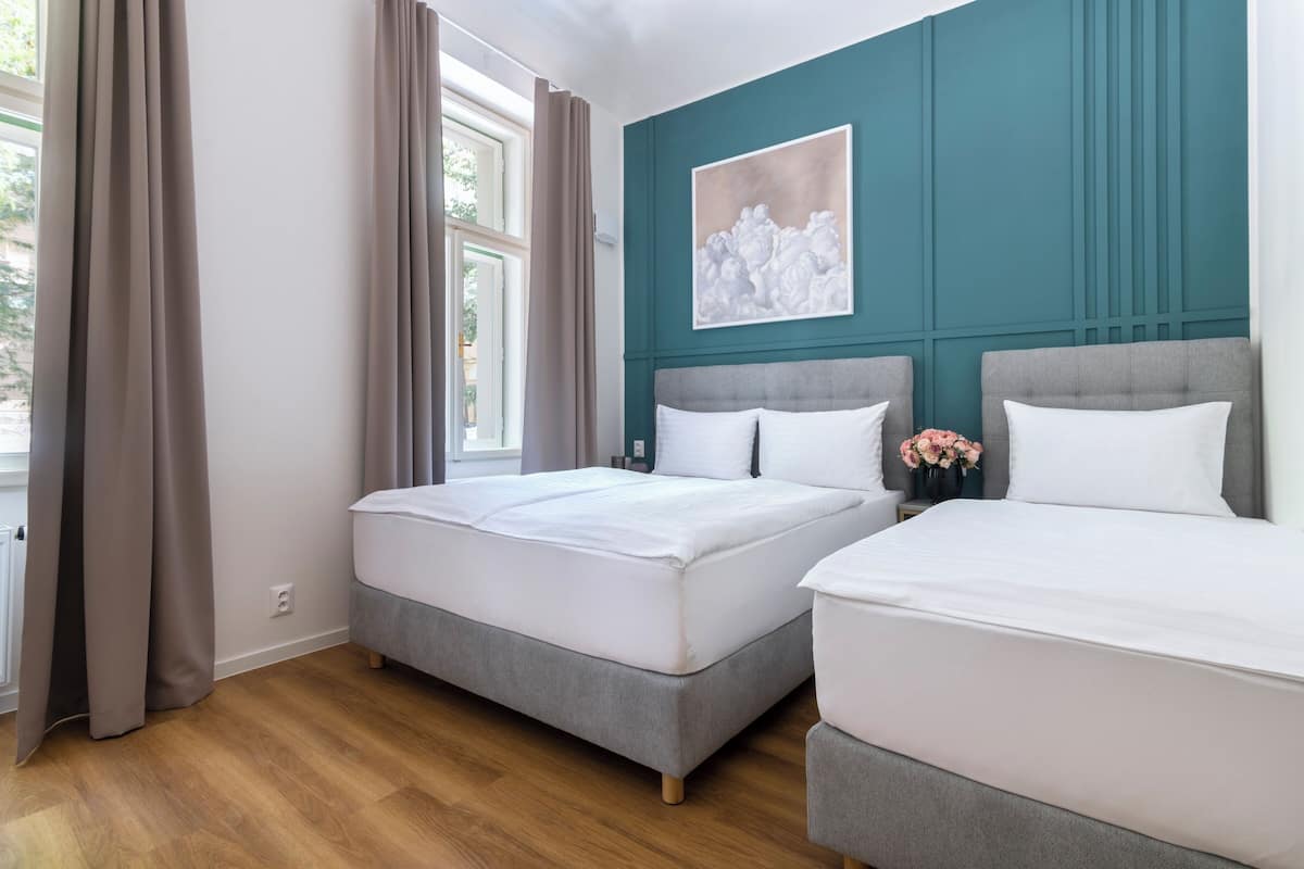 Ein Zimmer mit zwei Betten, einem Vorhangfenster, einer turquoise farbenen Akzentwand und einem weißen Kunstwerk.