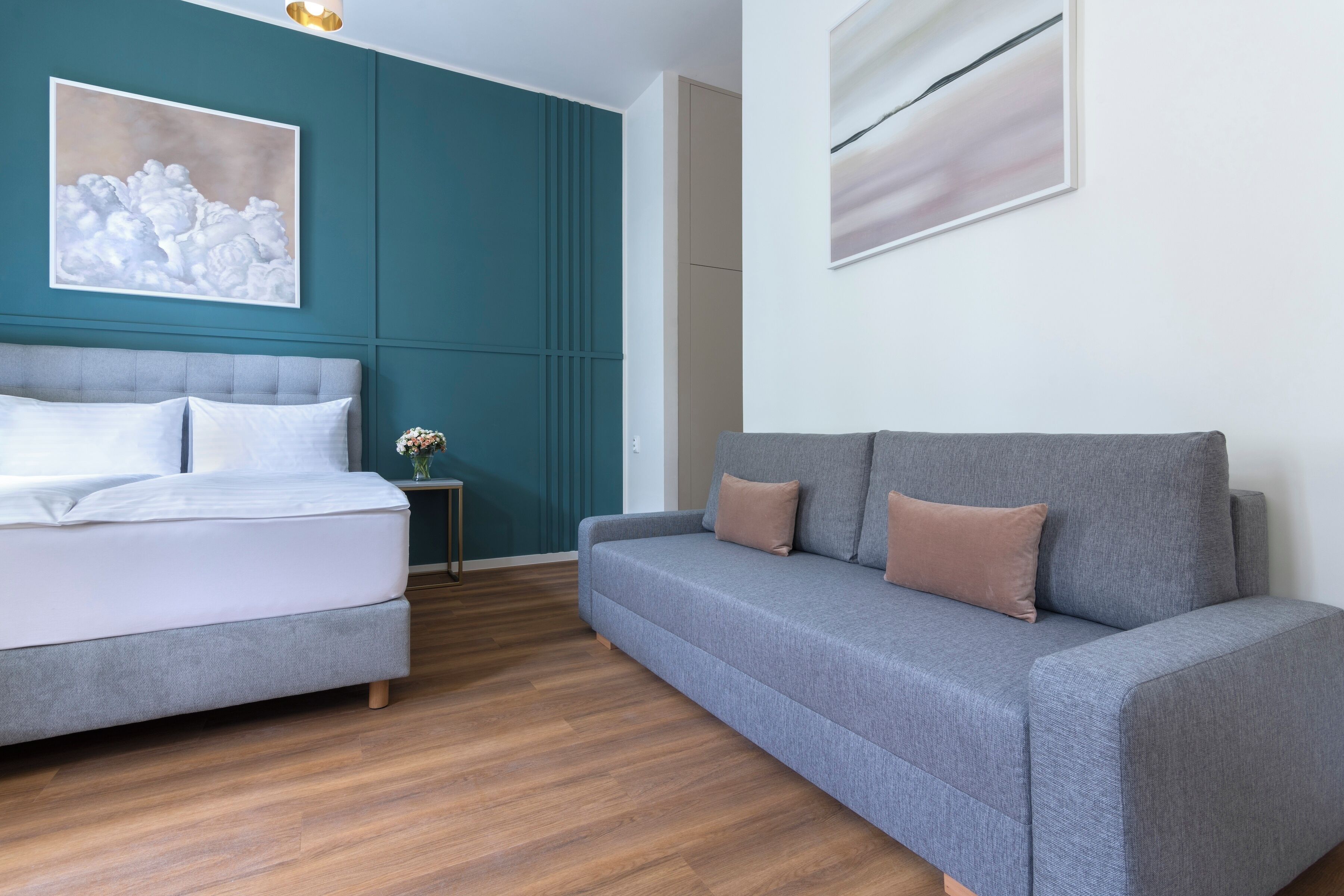 Un dormitorio moderno con una cama, un sofá gris, paredes color turquesa y suelo de madera.