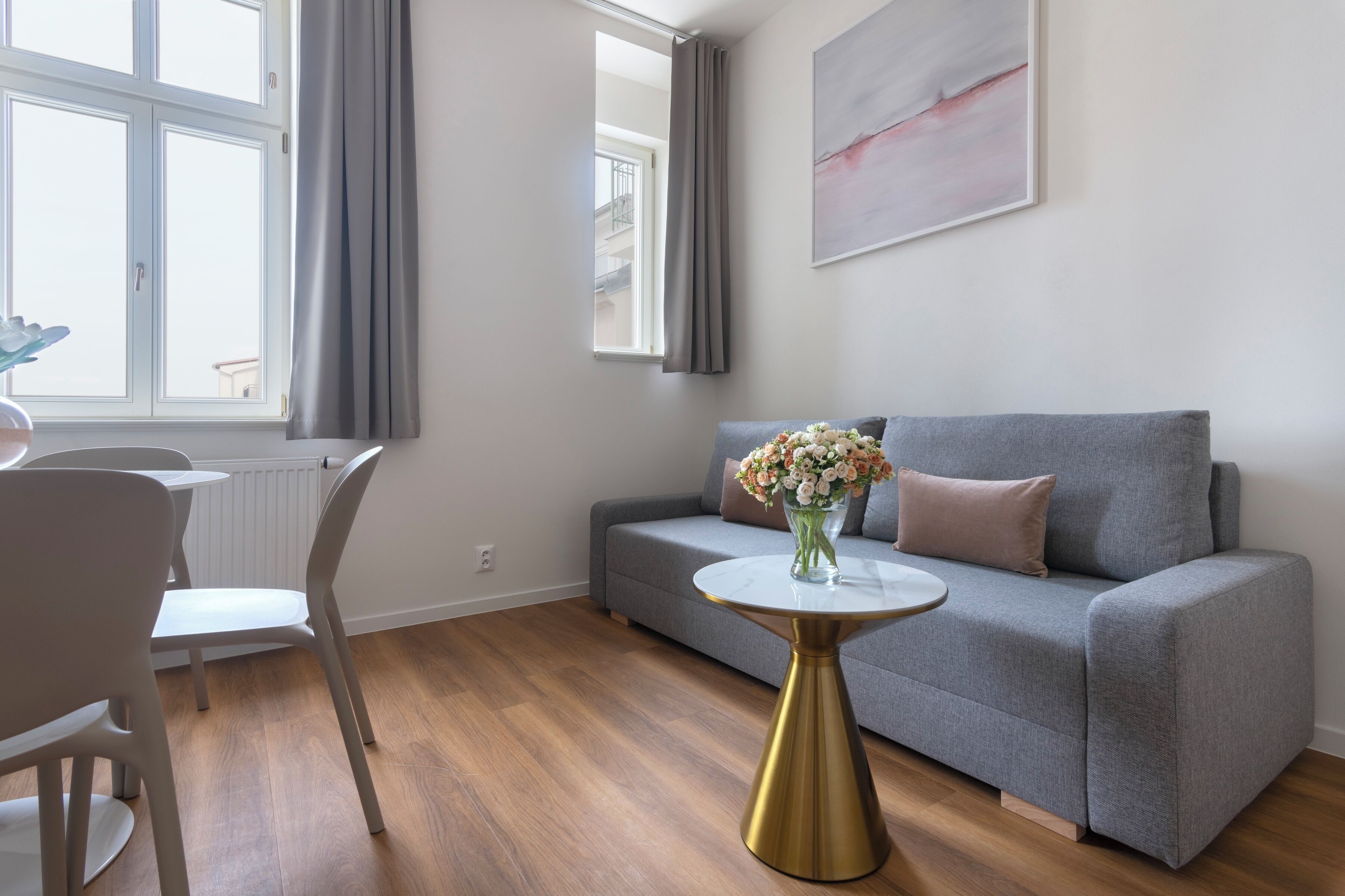 Una sala de estar moderna con un sofá gris, una mesa redonda con base dorada y un florero con flores.