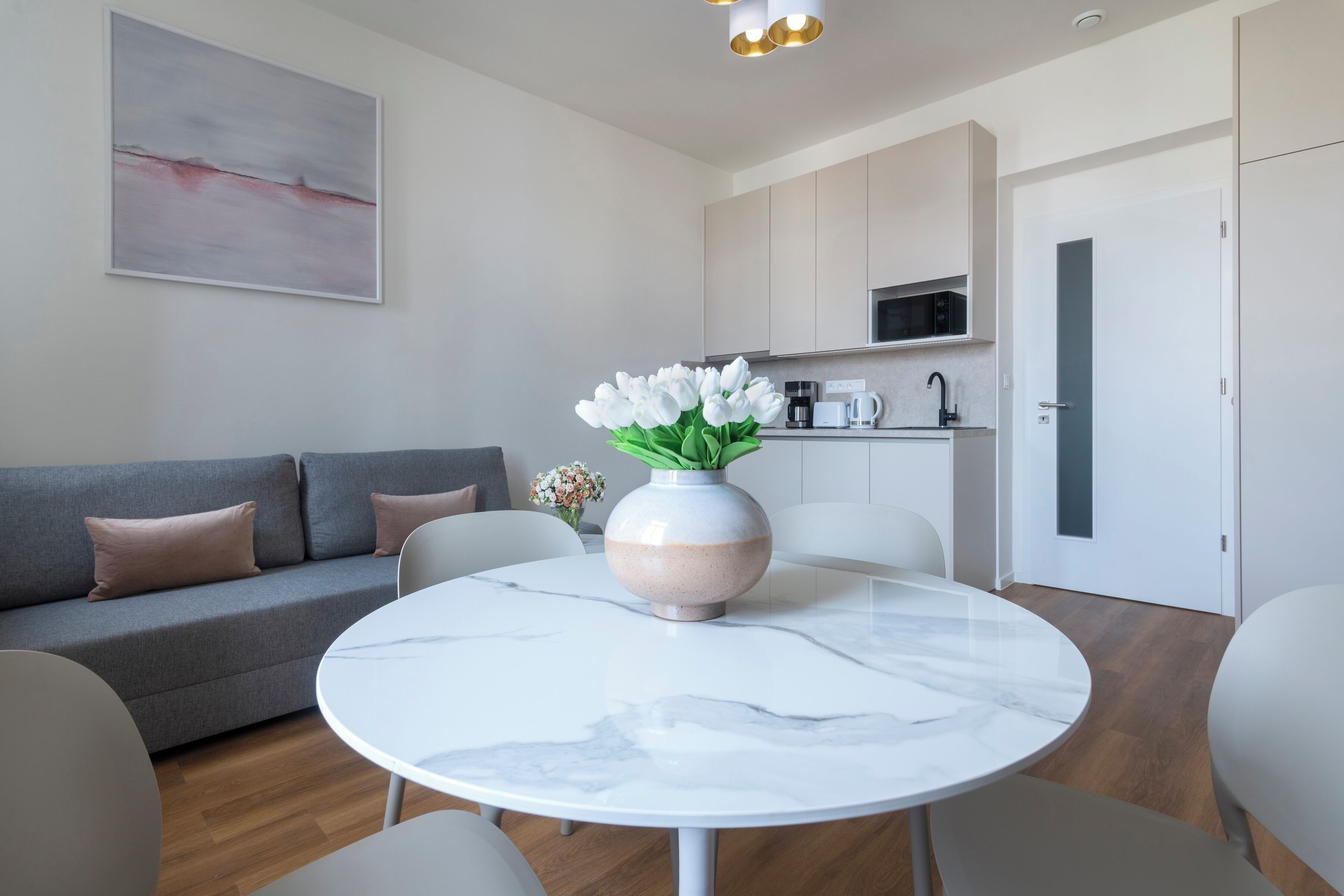 A modern living room with a round marble table, grey sofa, and a vase of white flowers.