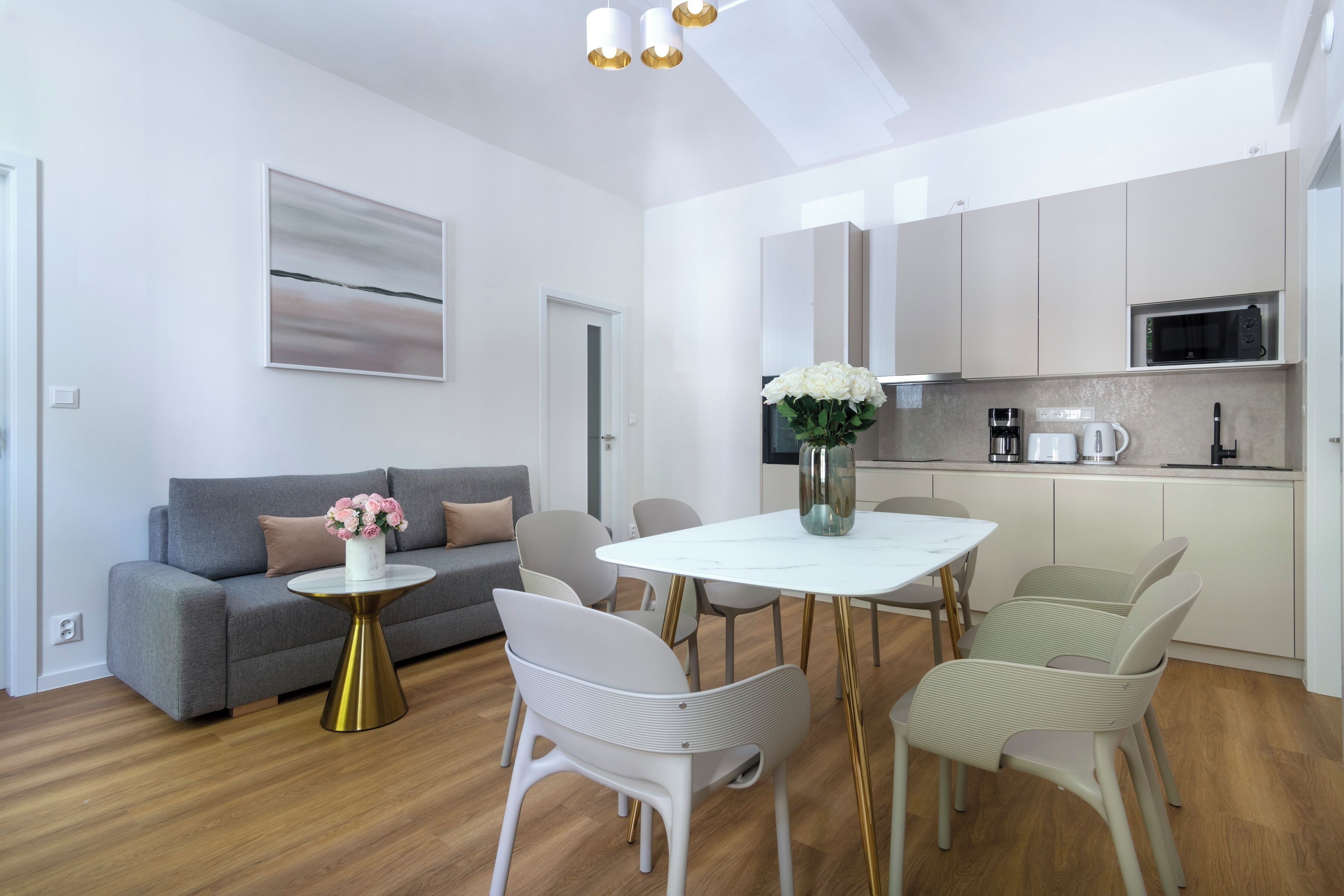 A modern living room with a grey sofa, white chairs, a white dining table, and a small gold side table.