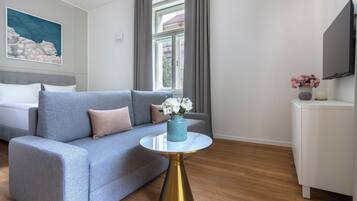 Een moderne hotelkamer met een grijze bank, een ronde gouden tafel en een televisie aan de muur.