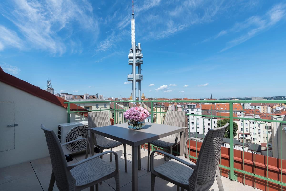 Ein Balkon mit Tisch und Stühlen, einer Blumenvase und Blick auf einen Turm sowie Gebäude.