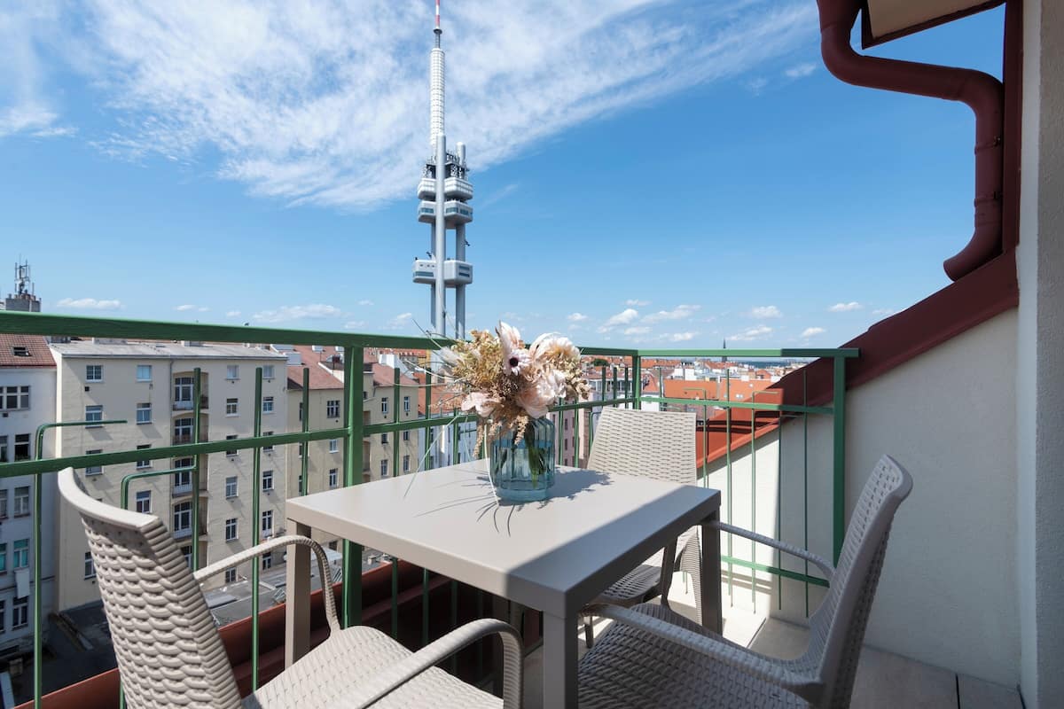 Ein Balkon mit Tisch und Stühlen, eine Vase mit Blumen und Blick auf einen Turm sowie Gebäude.