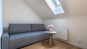 Una sala de estar moderna con un sofá gris, una mesita redonda con un florero y un tragaluz.