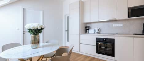 Una cocina moderna con armarios blancos, horno integrado y un comedor con mesa y sillas de mármol.