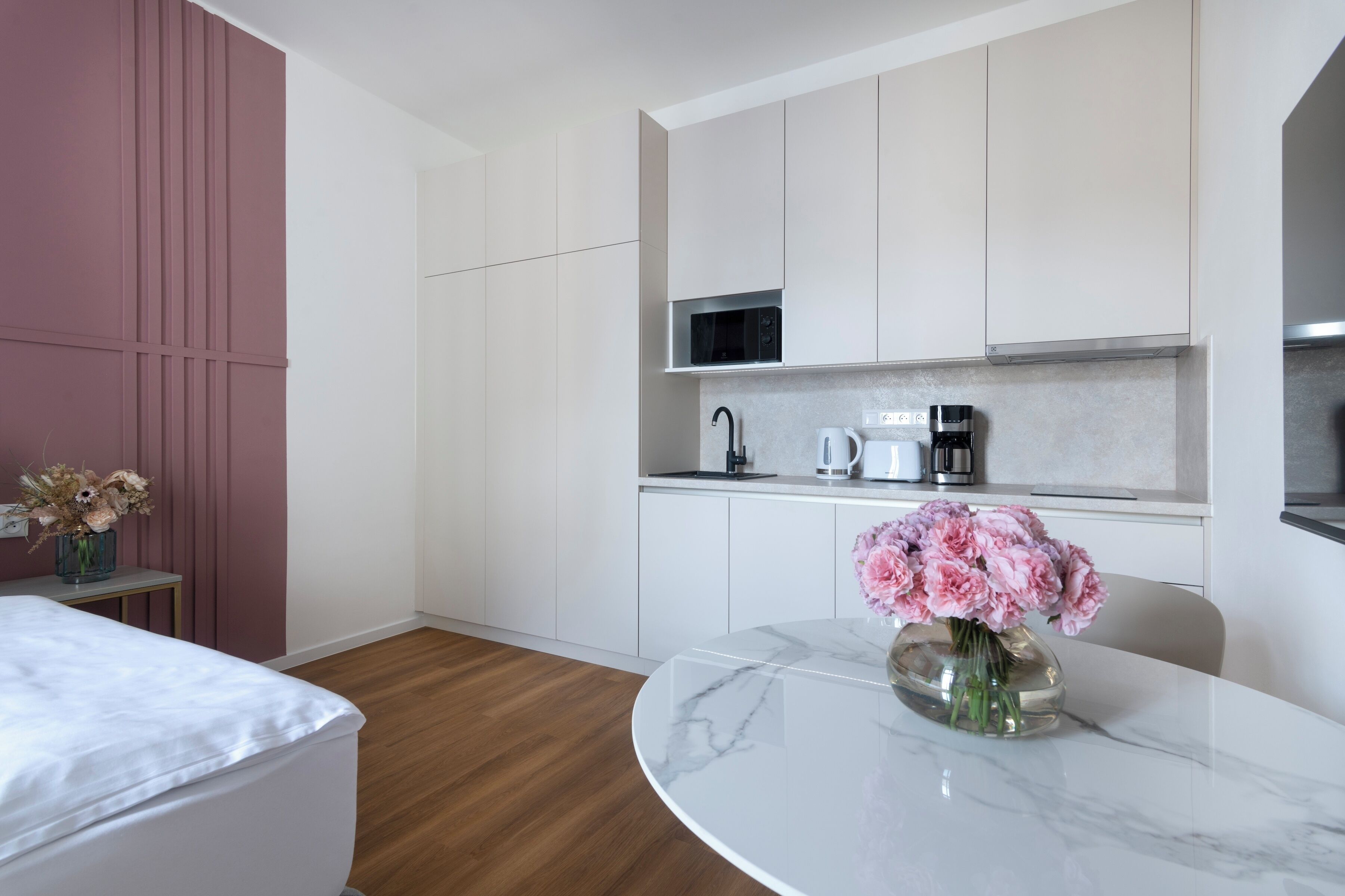 A compact kitchen with white cabinets, a microwave, a coffee maker, and a vase with flowers on the counter.