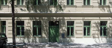 A building with a green door and multiple windows, a bench, and a tree in front.