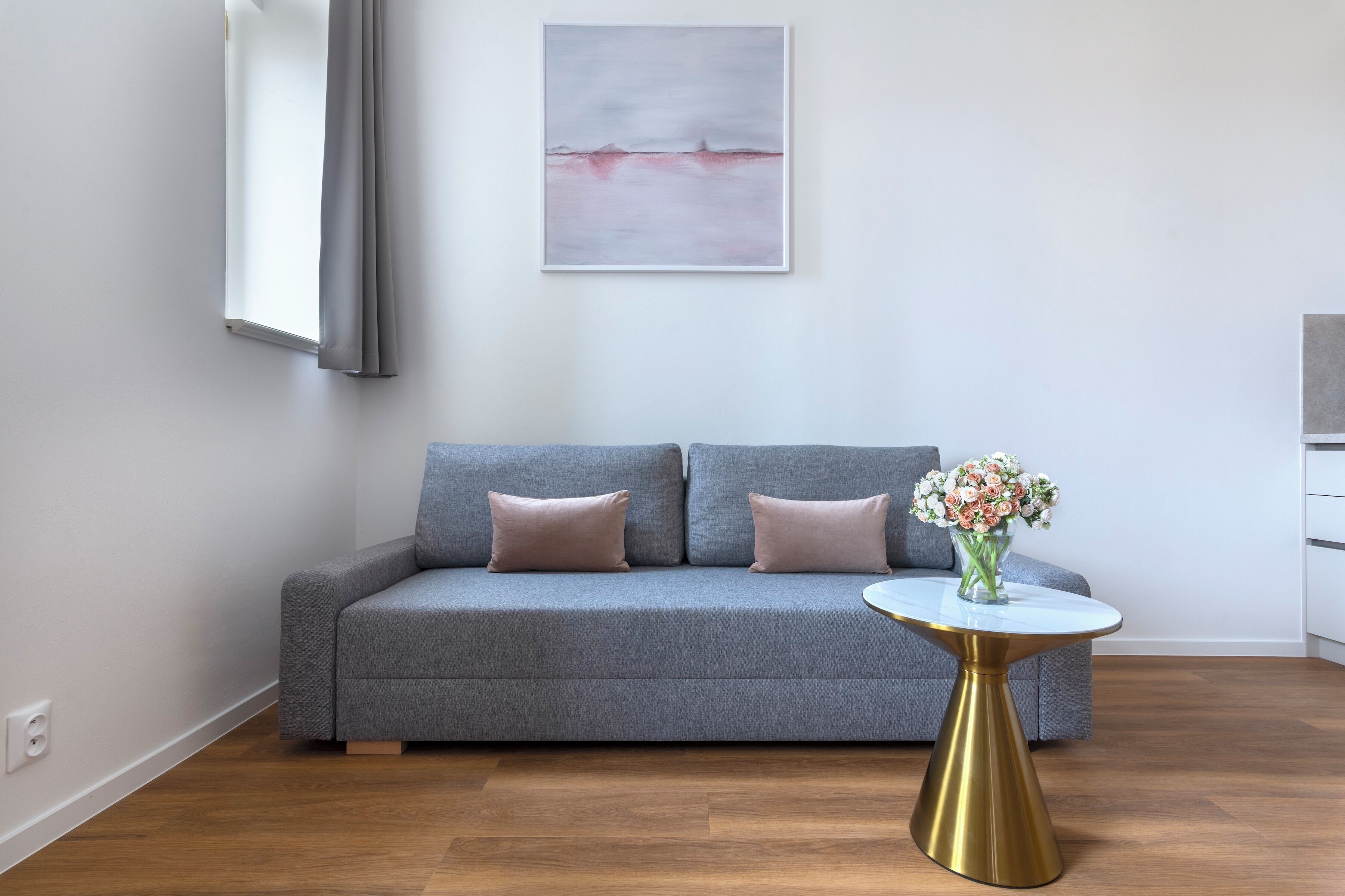 Una sala de estar moderna con un sofá gris, una mesa de centro redonda con base dorada, y un cuadro abstracto enmarcado en la pared.