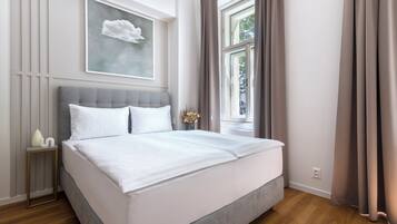 Un lit bien fait, avec du linge de lit blanc, dans une chambre moderne dotée d’une tête de lit grise, d’une œuvre d’art encadrée au mur et d’une fenêtre avec des rideaux.