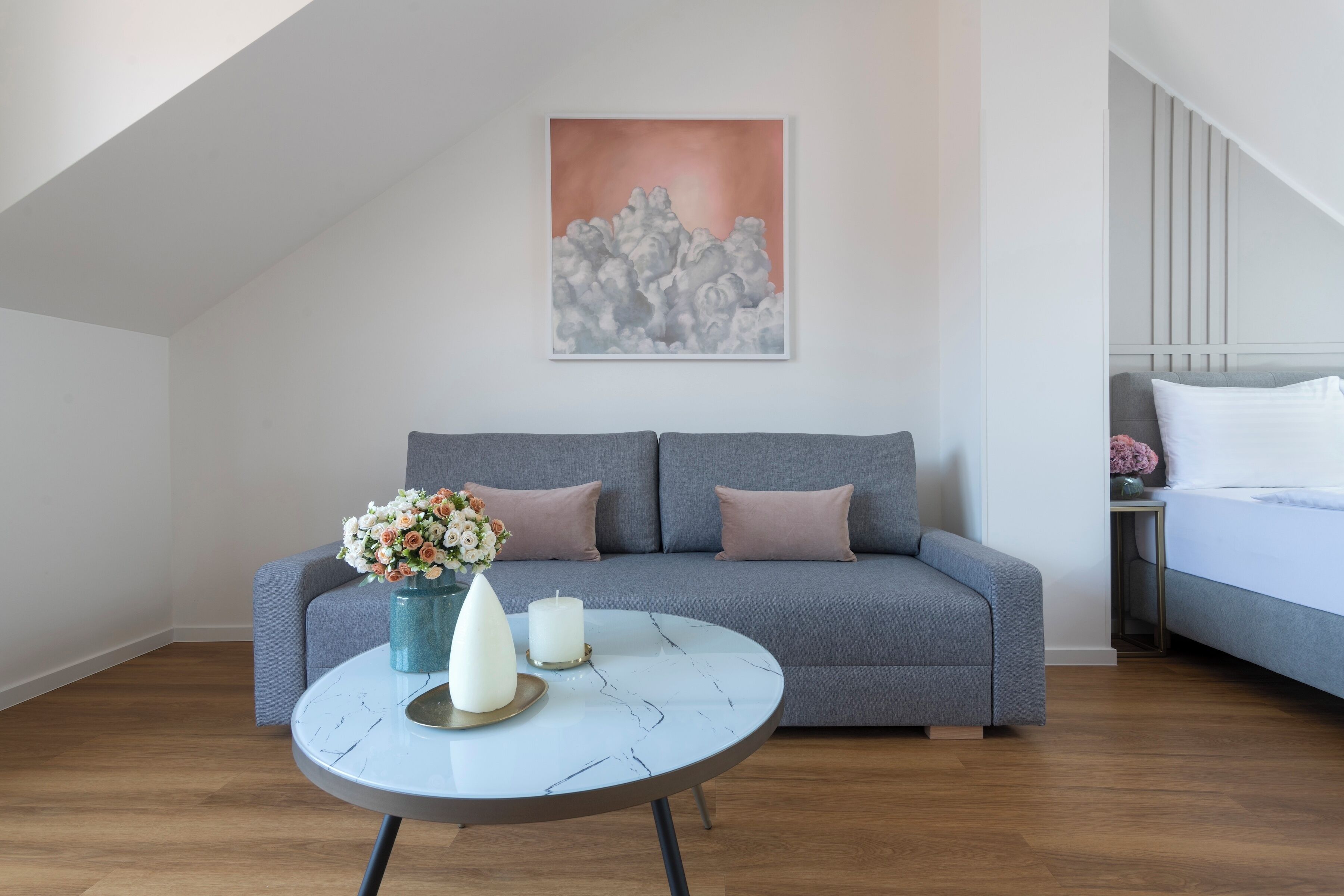 A modern living room with a grey sofa, a round coffee table with a vase of flowers, and a painting on the wall.