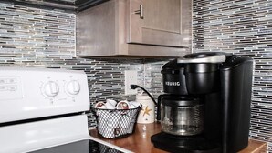 Una cocina con cafetera, un cesto de cápsulas de café y un hervidor sobre la encimera.