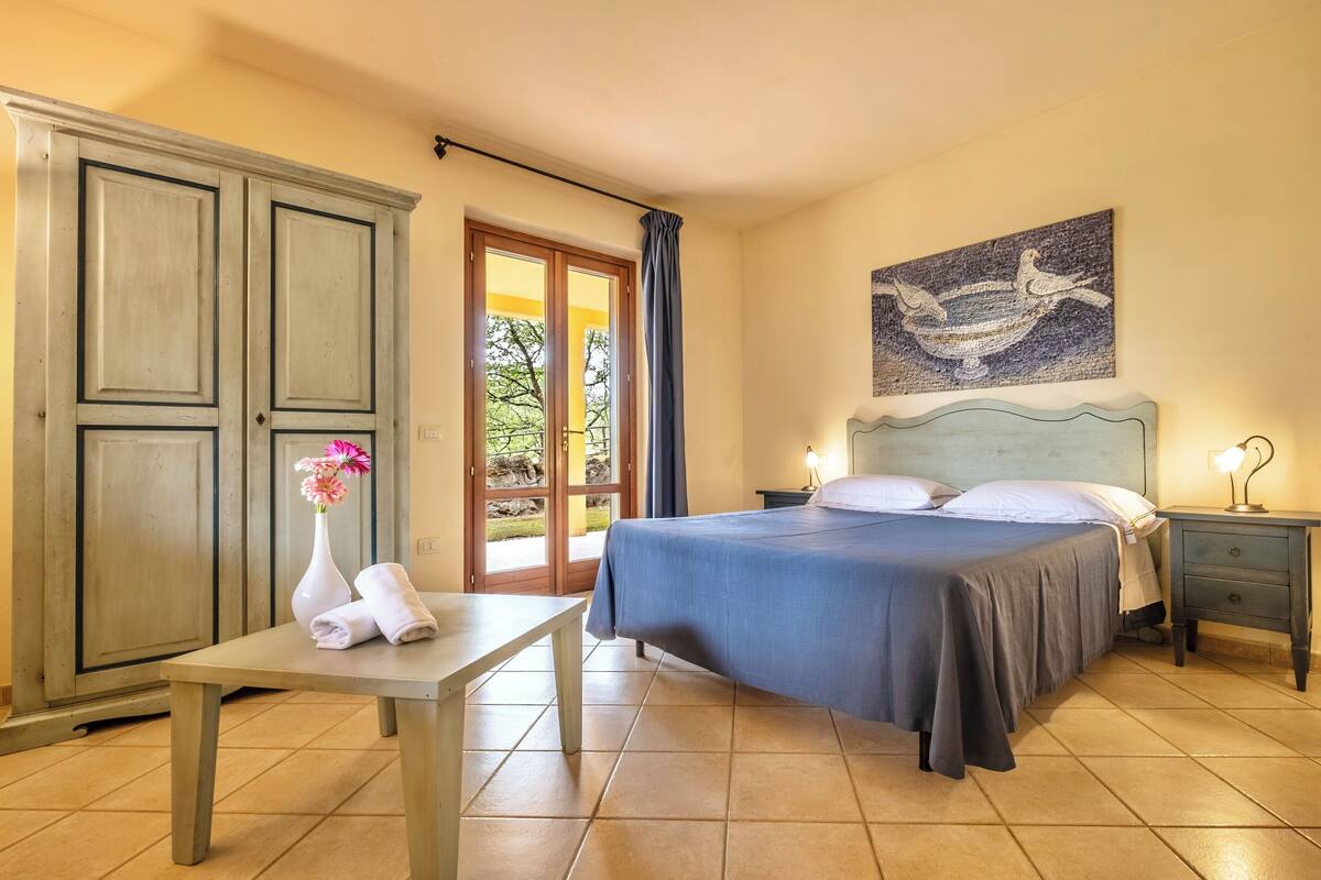 Un dormitorio con cama, mesita de noche, mesa y un cuadro en la pared.