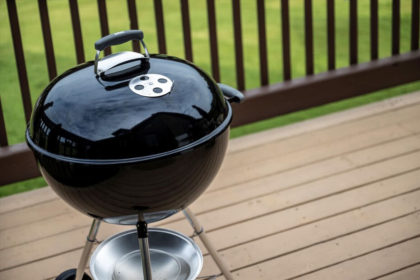 A black barbecue grill with a lid and a handle on a wooden deck.
