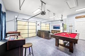 Un grand espace intérieur comprenant une table de billard, un baby-foot, un canapé et un téléviseur.