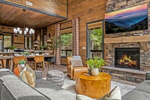 A modern log cabin interior with a stone fireplace, a dining area, and a cozy seating area.
