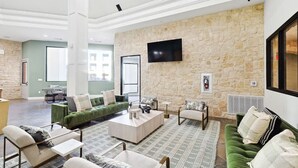 A spacious living area with a stone wall, a flat-screen TV, and multiple seating options including a green sofa and armchairs. - Stylish 2B near Legacy West  Wi-Fi, Fitness, Pool (Frisco)