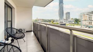 A balcony with a view of modern buildings, a chair, and a table with a magazine. - Stylish Apartment with a Balcony | Air Conditioning (Rzeszów)