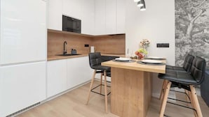 A modern kitchen with white cabinets, a wooden countertop, and a dining area with two black chairs and a wooden table. - Stylish Apartment with a Balcony | Air Conditioning (Rzeszów)