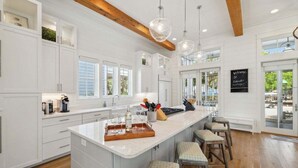 A spacious kitchen with white cabinetry, a large island with bar stools, pendant lighting, and a chalkboard sign. - Next to Camp WaterColor! Sleeps 22! Pool, Gym, LSV, Bikes & Carriage House! (Santa Rosa Beach)